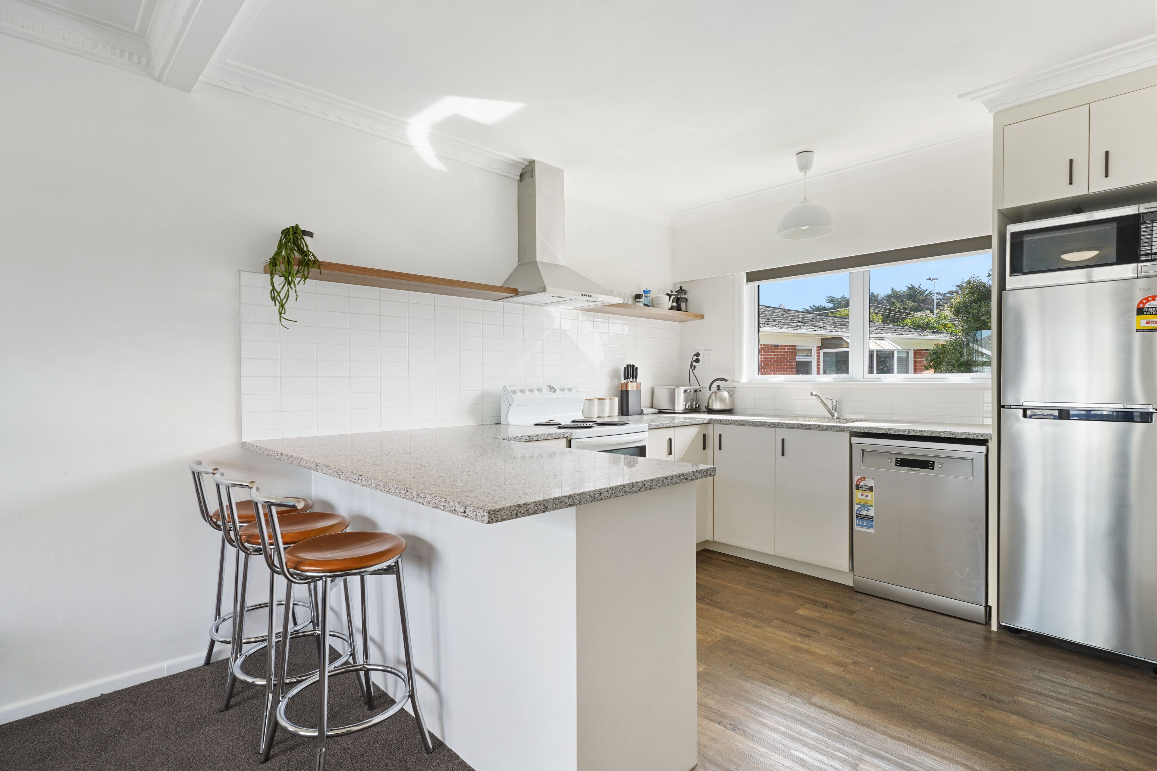 A modern kitchen with white cabinetry, stainless steel appliances, and a bar area with stools.