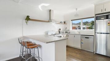 A modern kitchen with white cabinetry, stainless steel appliances, and a bar area with stools.