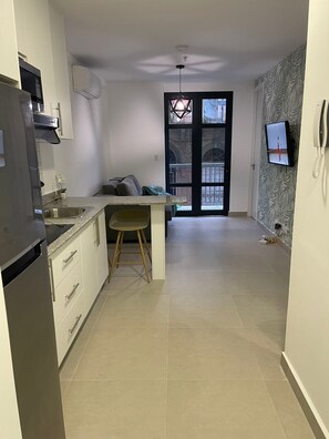A modern kitchen with a built-in refrigerator, a dining area with a wooden chair, and a large window with a view of a courtyard.