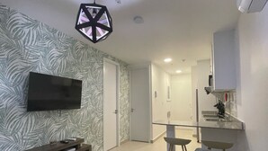 A modern living room with a flat-screen TV, a geometric pendant light, a sofa, and a kitchen area with a sink and countertop. - 2Rcondo balcony Surrounded by history with Modern Amenities (Panama City)