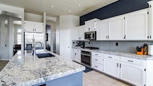 Una cucina moderna con mobili bianchi, piani di lavoro in granito, elettrodomestici in acciaio inossidabile e faretti a soffitto.