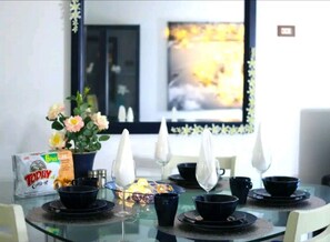 A dining area with a glass table set for a meal, featuring a bowl of cereal and a box of cereal on the table.