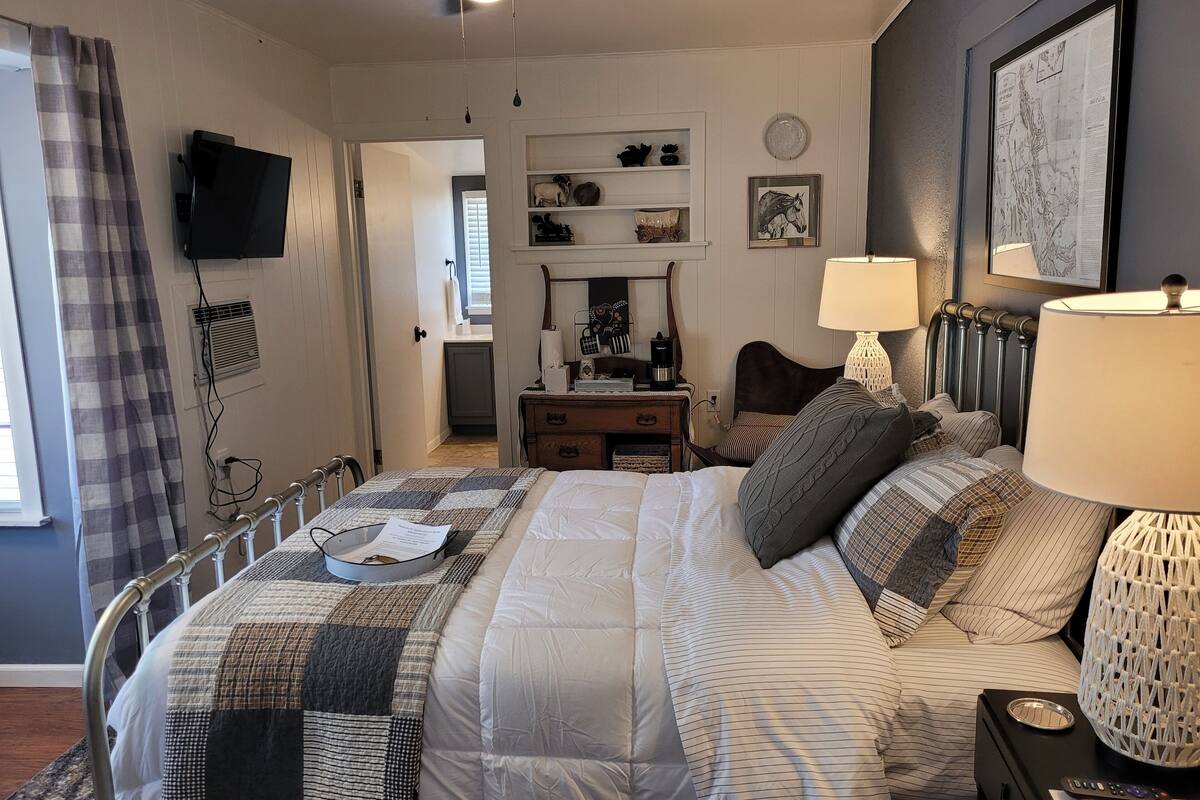 A bedroom with a bed, bedside lamps, a dresser, a TV, and a map on the wall.