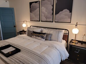 A neatly made bed with a black tray, two bedside tables with lamps, and artwork on the wall. - Mountainside Inn (Fort Davis)