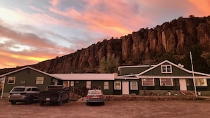 A two-story building with a flat roof and a chimney, surrounded by a dirt lot with parked vehicles. - Mountainside Inn (Fort Davis)