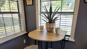 A small wooden table with two stools, a potted plant, and two white cups on a window sill. - Mountainside Inn (Fort Davis)