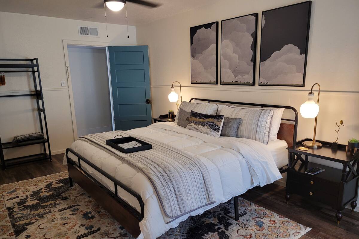 A neatly arranged bedroom with a bed, bedside tables, a wall-mounted shelf, and a door.