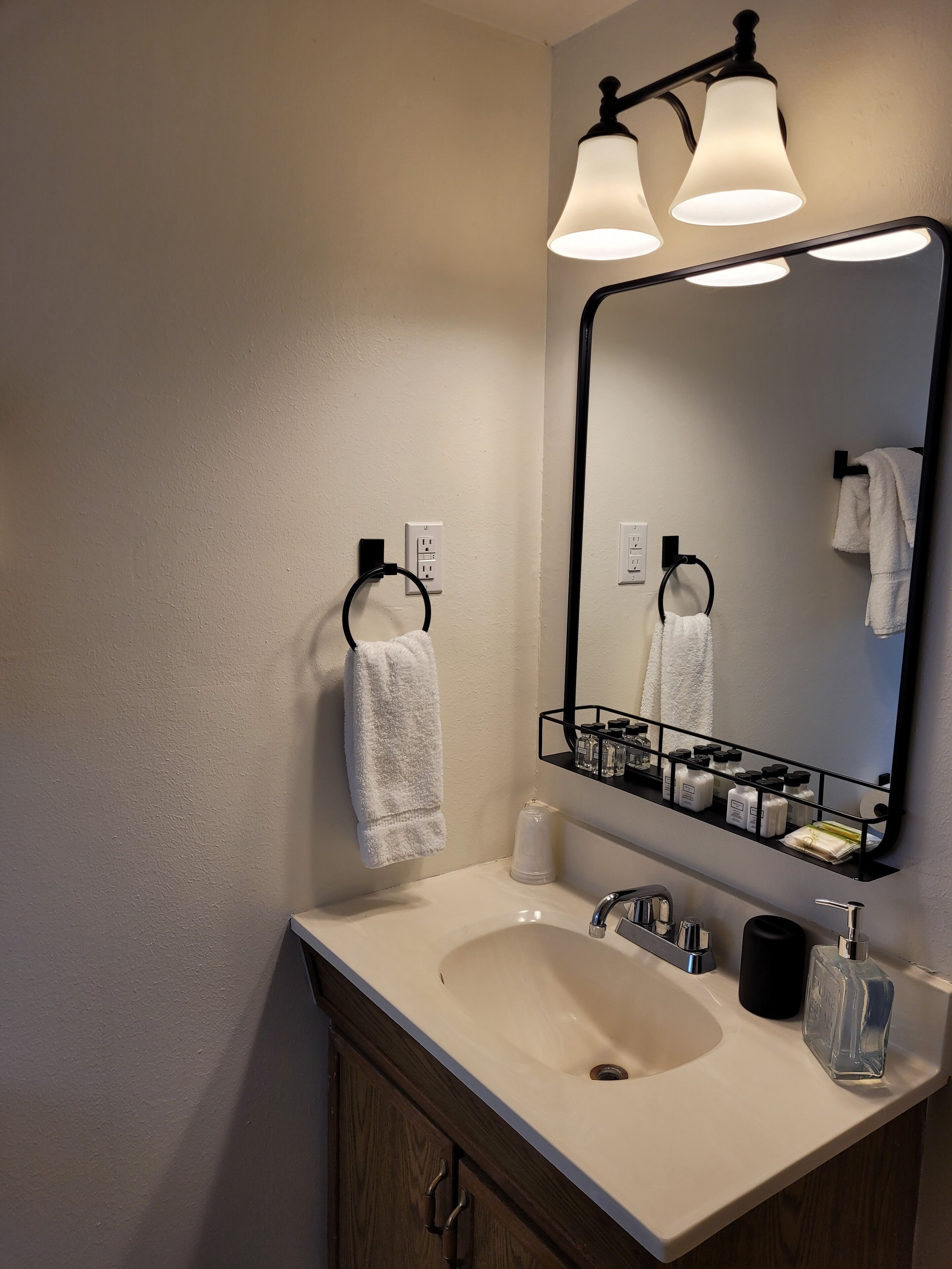 A bathroom with a sink, mirror, towel rack, and toiletries.