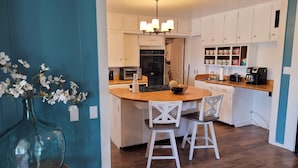 A modern kitchen with white cabinets, a wooden island, two bar stools, and a vase of flowers. - Mountainside Inn (Fort Davis)