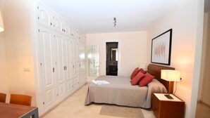 Un dormitorio con cama, mesita de noche, lámpara, armario y un cuadro en la pared.