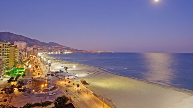 Paisaje costero nocturno con playa, edificios iluminados y cielo despejado.