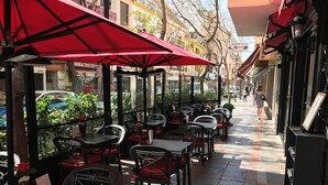 Café al aire libre con sombrillas rojas, sillas negras y suelo de baldosas.