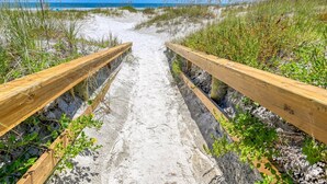 Un sentier de plage sablonneux, bordé de rambardes en bois, qui mène à l’océan.