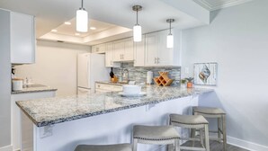 Une cuisine moderne avec des armoires blanches, un comptoir en granit et trois suspensions lumineuses.