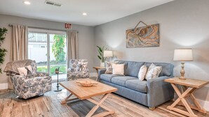 Un salón con un sofá gris, sillones estampados, una mesa de centro de madera y dos mesitas de noche con lámparas.