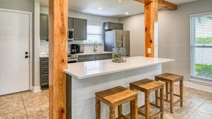 Una cocina moderna con una isla blanca, taburetes de madera y vistas al exterior a través de amplios ventanales.