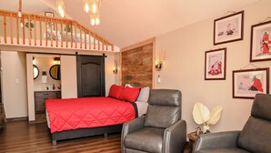 Ein Schlafzimmer mit einem Bett, zwei Ledersesseln, einer Holzbalkendecke und Kunstwerken an den Wänden.