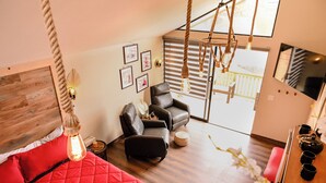 Ein modernes Zimmer mit einem roten Bett, einem Ledersessel, Holzboden und einer Pendelleuchte.