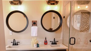 Ein Badezimmer mit zwei Spiegeln, einem Waschbecken mit zwei Wasserhähnen und einer Duschkabine aus Glas.