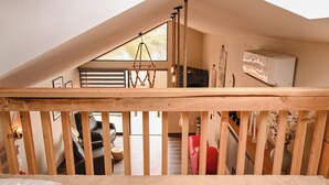 Ein Schlafzimmer im Loft-Stil mit schrägem Dach, Holzbalkon, einer Pendelleuchte und Blick auf den Wohnbereich darunter.