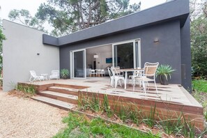 Een modern huis met een patio, voorzien van tuinmeubilair en een grote schuifpui die leidt naar de binnenruimte.