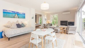 A modern living room with a white sofa, a dining table with chairs, a TV, and a fireplace. - Coolart Studios: Studio Two (Balnarring)