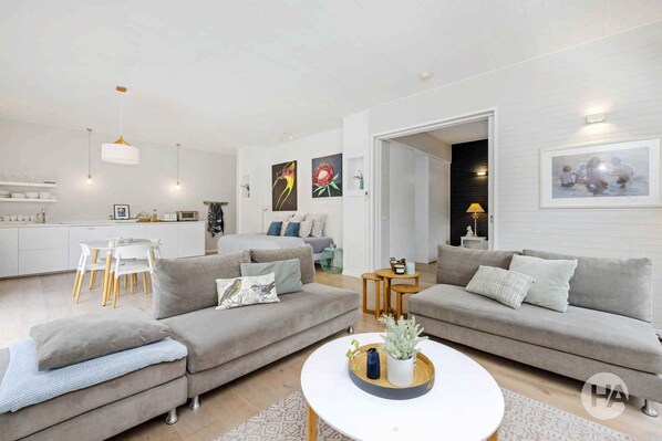 Een moderne woonkamer met twee grijze banken, een witte salontafel en een eethoek met een witte tafel en stoelen.