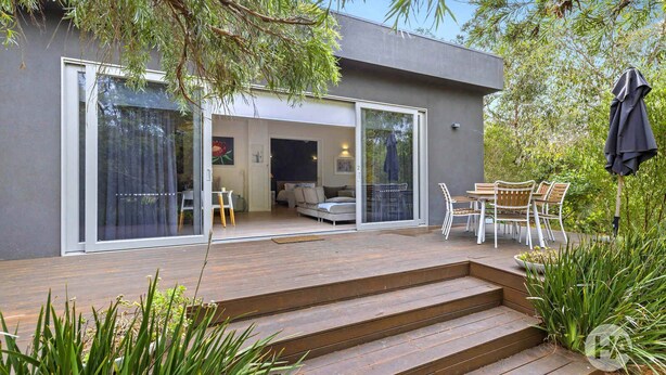 A modern house with a deck, sliding glass doors leading to an interior with a sofa and dining area. - Coolart Studios: Studio Two (Balnarring)
