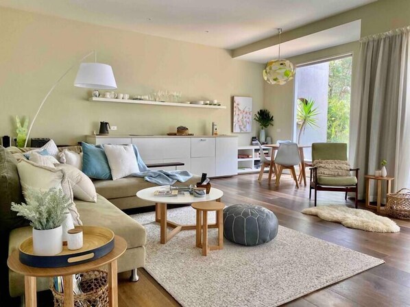 Een moderne woonkamer met een bank, salontafel, poef en een eethoek met stoelen en een tafel.