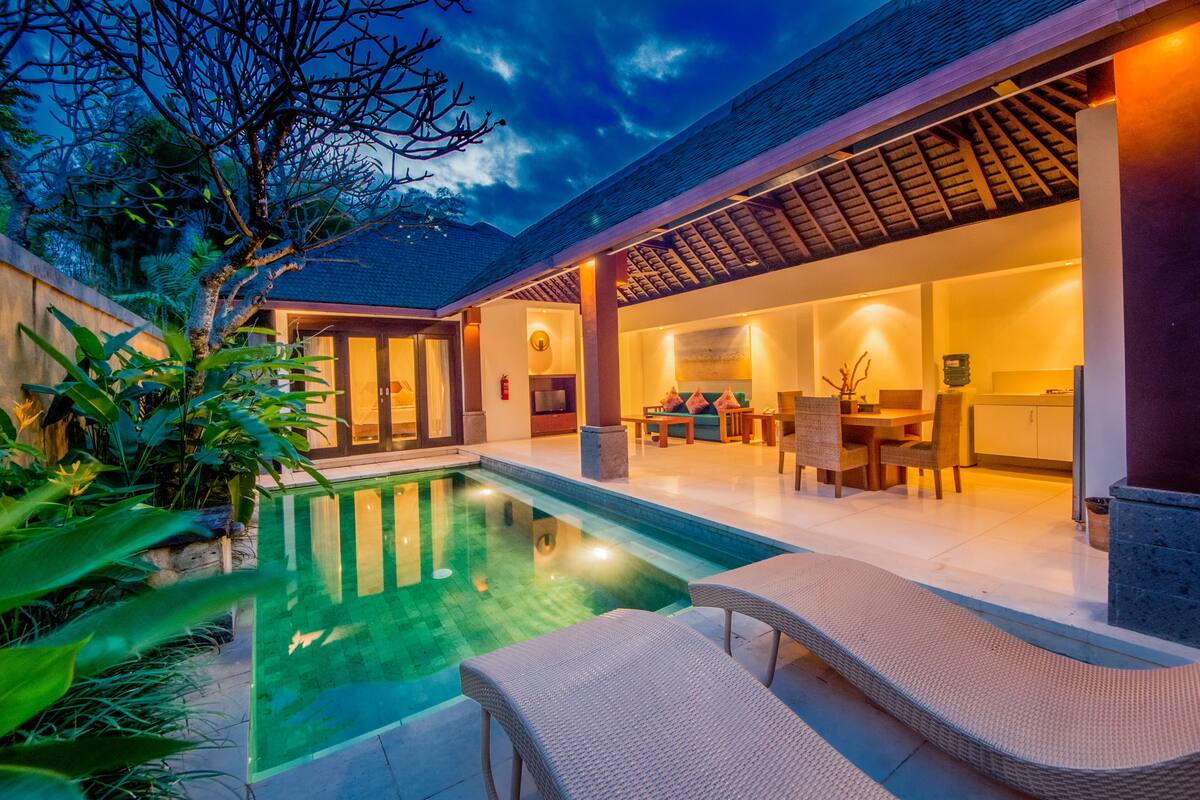A modern house with a swimming pool, outdoor seating, and a well-lit interior.