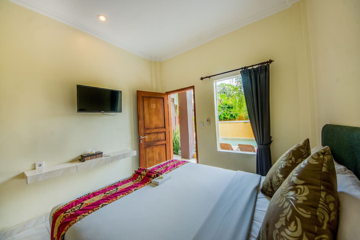 A hotel room with a bed, a mounted TV, a window with curtains, and a door leading outside.