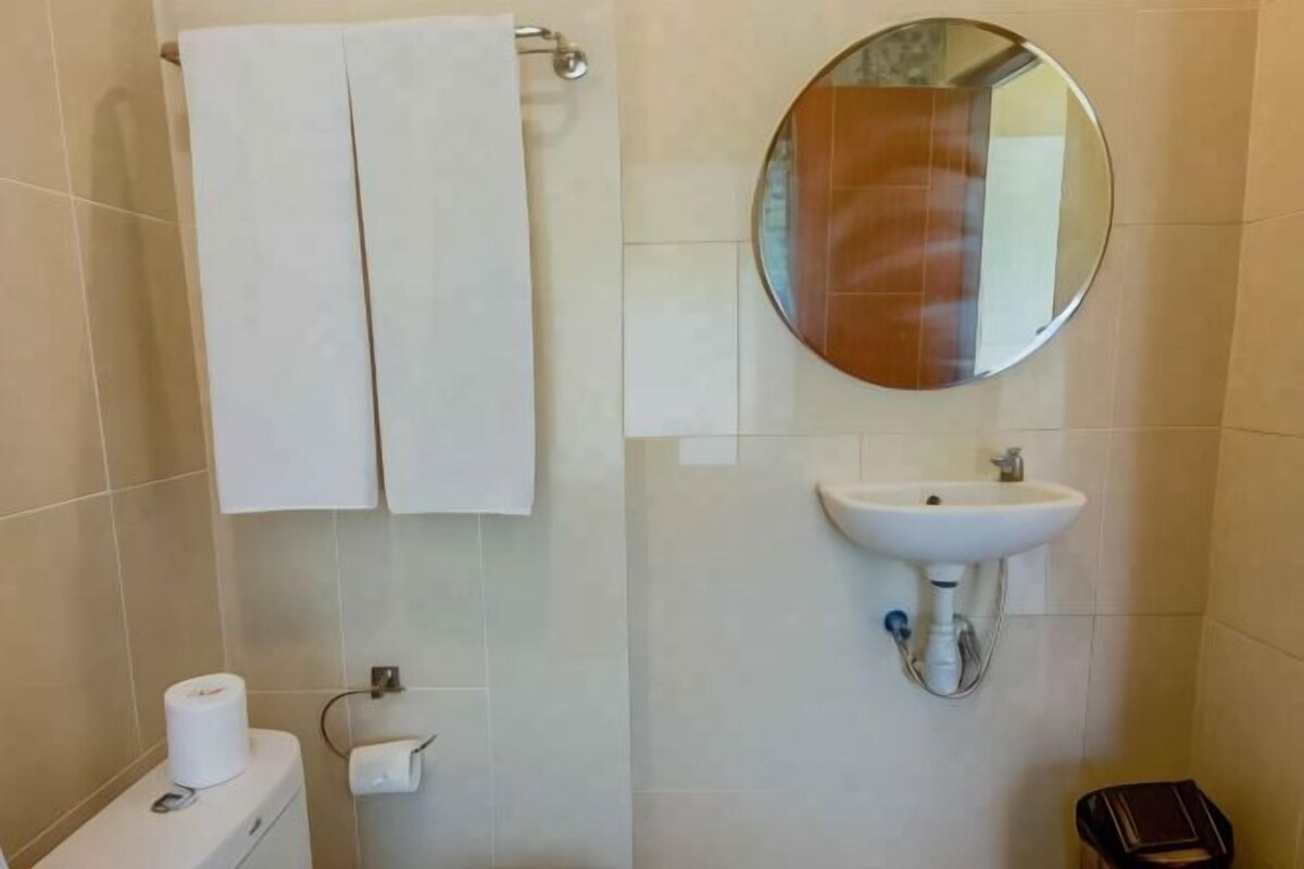 A bathroom with a toilet, two white towels, a sink, and a mirror.