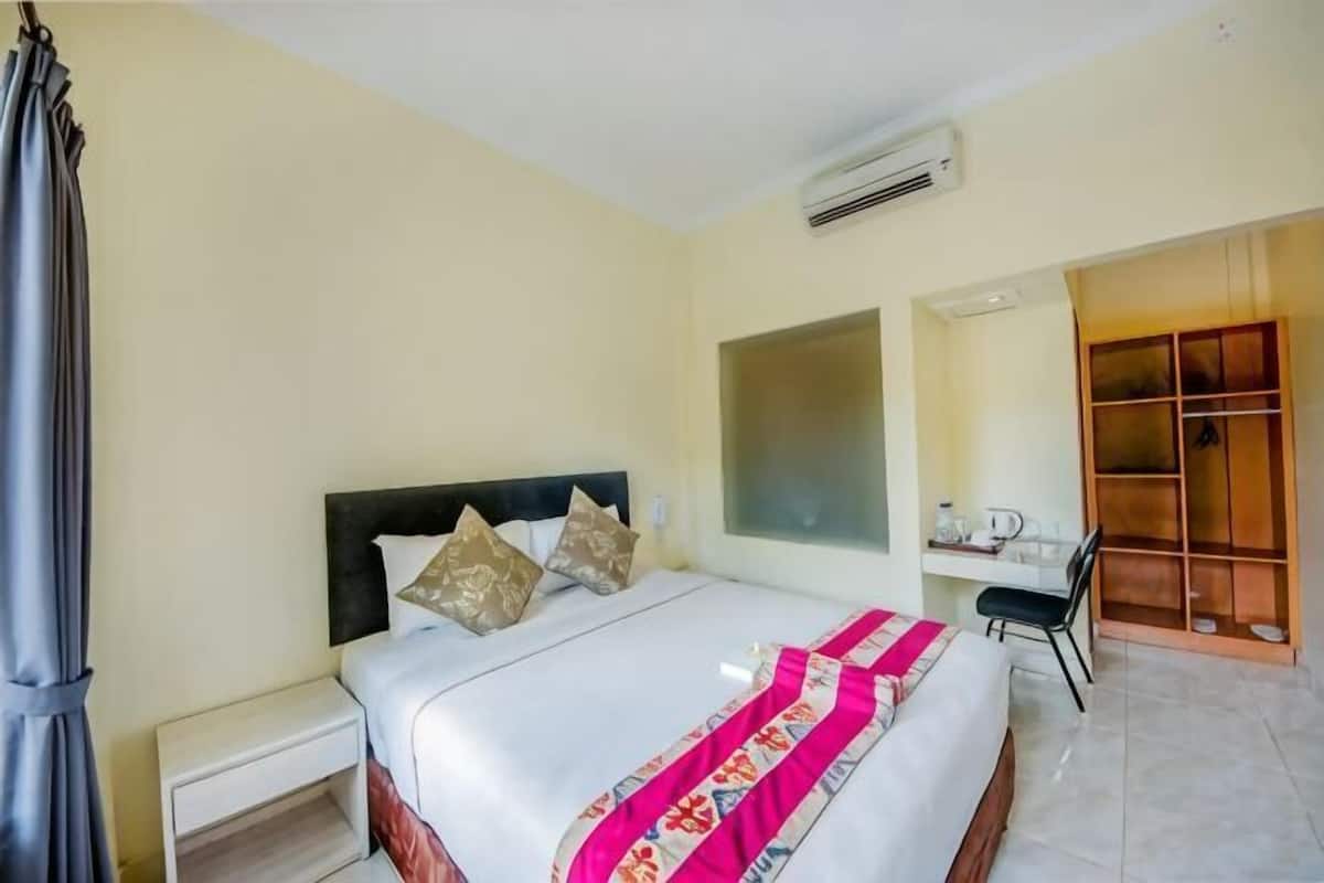 A hotel room with a bed, bedside table, chair, desk, and a wardrobe.