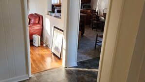 Ein Flur mit Steinboden, der in ein Wohnzimmer führt, mit einem roten Ledersessel, einem weißen Ventilator und einem gerahmten Bild.
