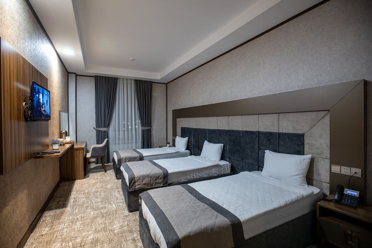 Une chambre d’hôtel avec trois lits, un bureau, une télévision et un téléphone sur la table de chevet.