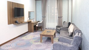 A hotel room with a wooden desk, a flat-screen TV, a grey sofa, and a patterned carpet. - Volga Hotel (Baku)
