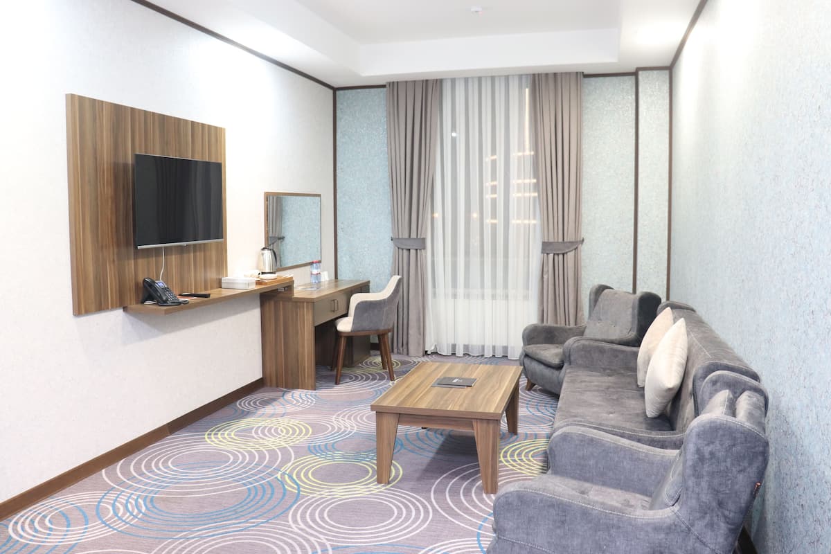 Une chambre d’hôtel avec un bureau en bois, un téléviseur à écran plat, un canapé gris et une moquette à motifs.