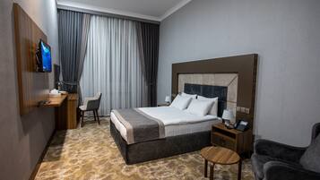 Een hotelkamer met een bed, een bureau, een stoel, een televisie en een klein tafeltje.