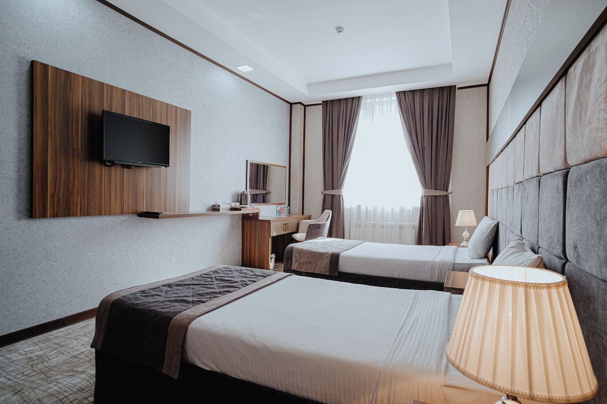 Une chambre d’hôtel avec deux lits, un téléviseur fixé au mur, un bureau avec une chaise et une fenêtre avec des rideaux.