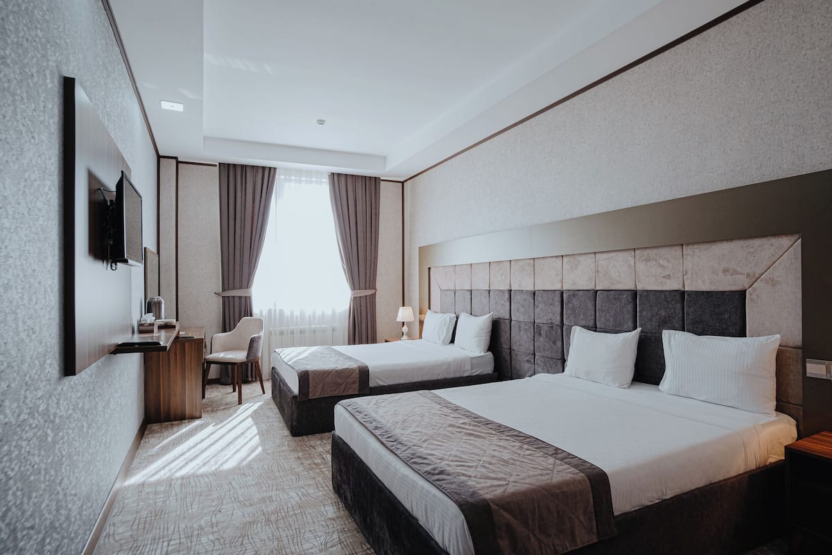 Une chambre d’hôtel moderne équipée de deux lits, d’un bureau, d’une chaise et d’une grande fenêtre avec des rideaux.