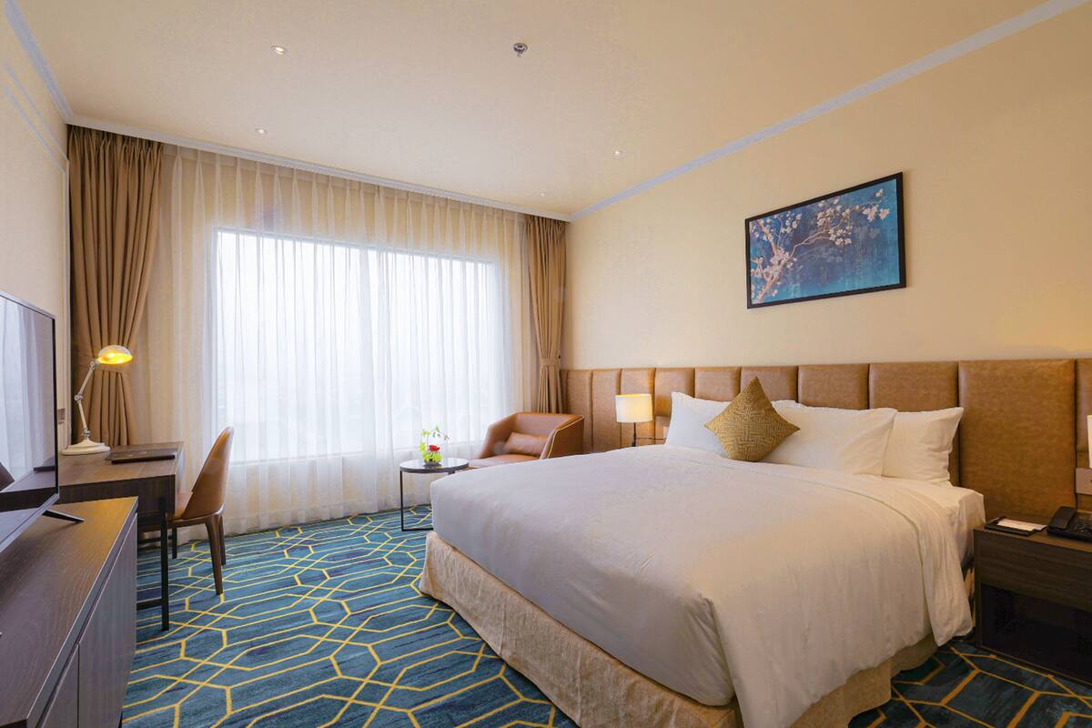 A hotel room with a large bed, a desk, a chair, a nightstand, and a painting on the wall.