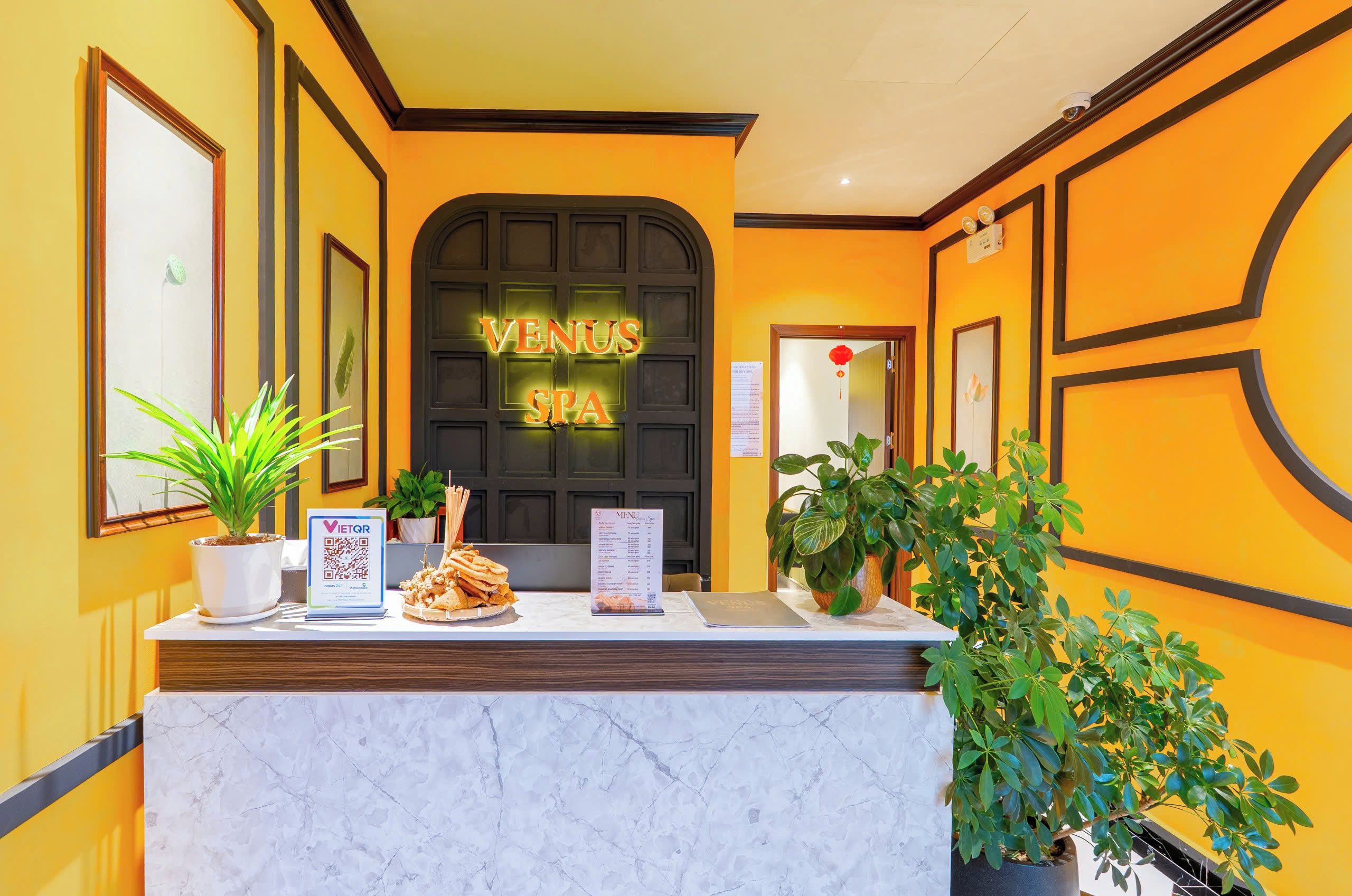 A reception desk with a neon sign reading 'VENUS SPA', a menu stand, and potted plants.