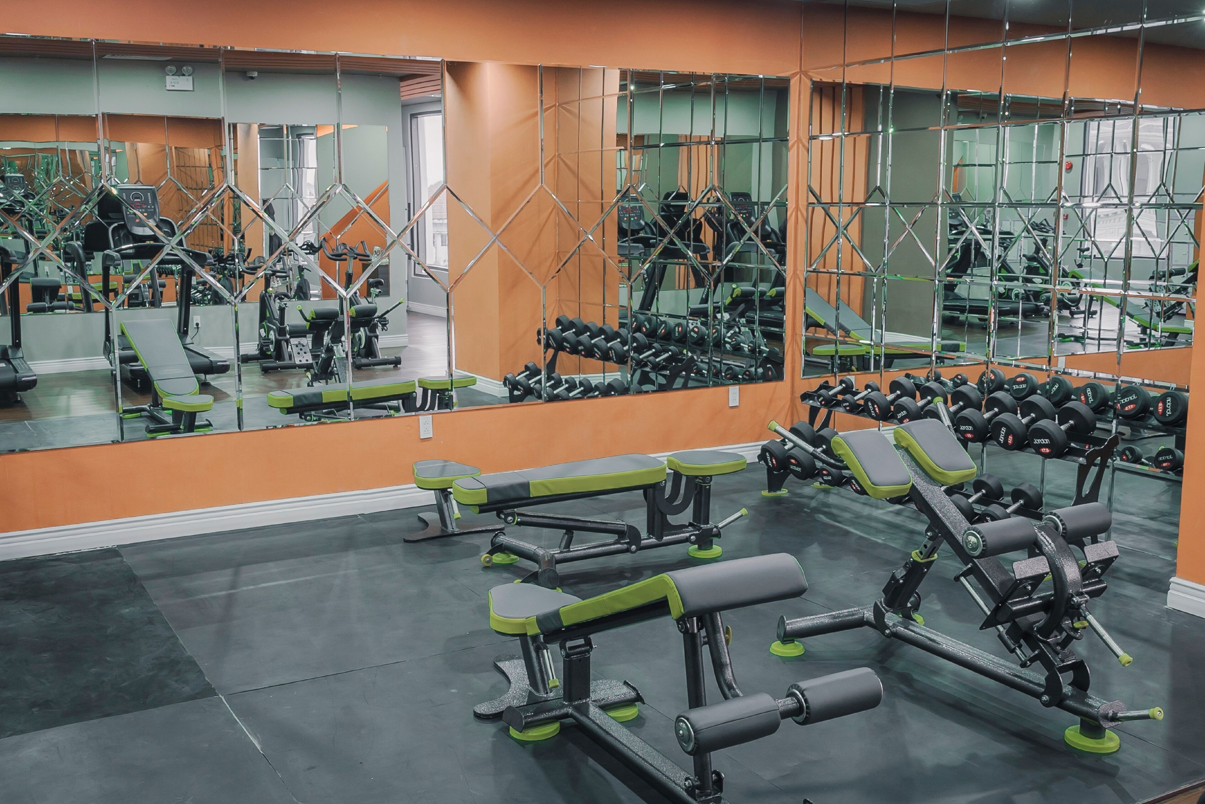 A gym with various exercise equipment, mirrors, and orange walls.