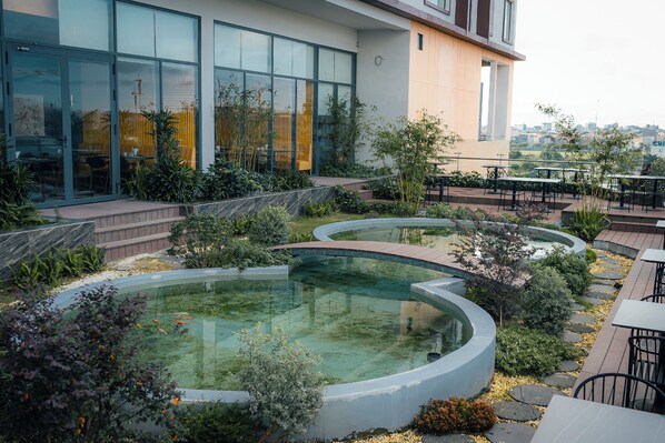 A rooftop garden with circular water features, outdoor seating, and a building with large windows.