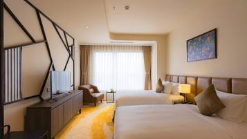 Een hotelkamer met twee bedden, een bureau, een flatscreen-tv, een stoel, een klein tafeltje en een schilderij aan de muur.