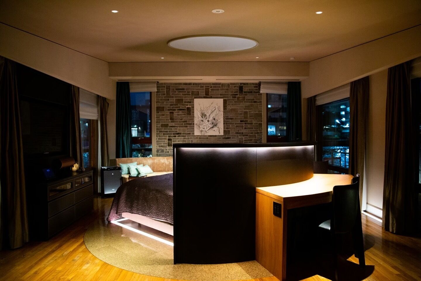 A modern bedroom with a bed, a desk, and a view of the city at night.