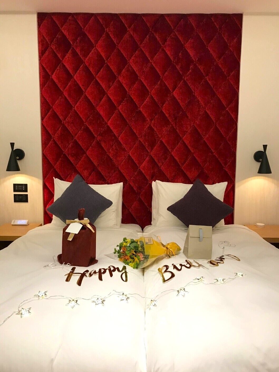 Une chambre d’hôtel avec une tête de lit rouge matelassée, deux oreillers, une table de chevet avec une lampe et une autre table de chevet avec un panneau de commande.