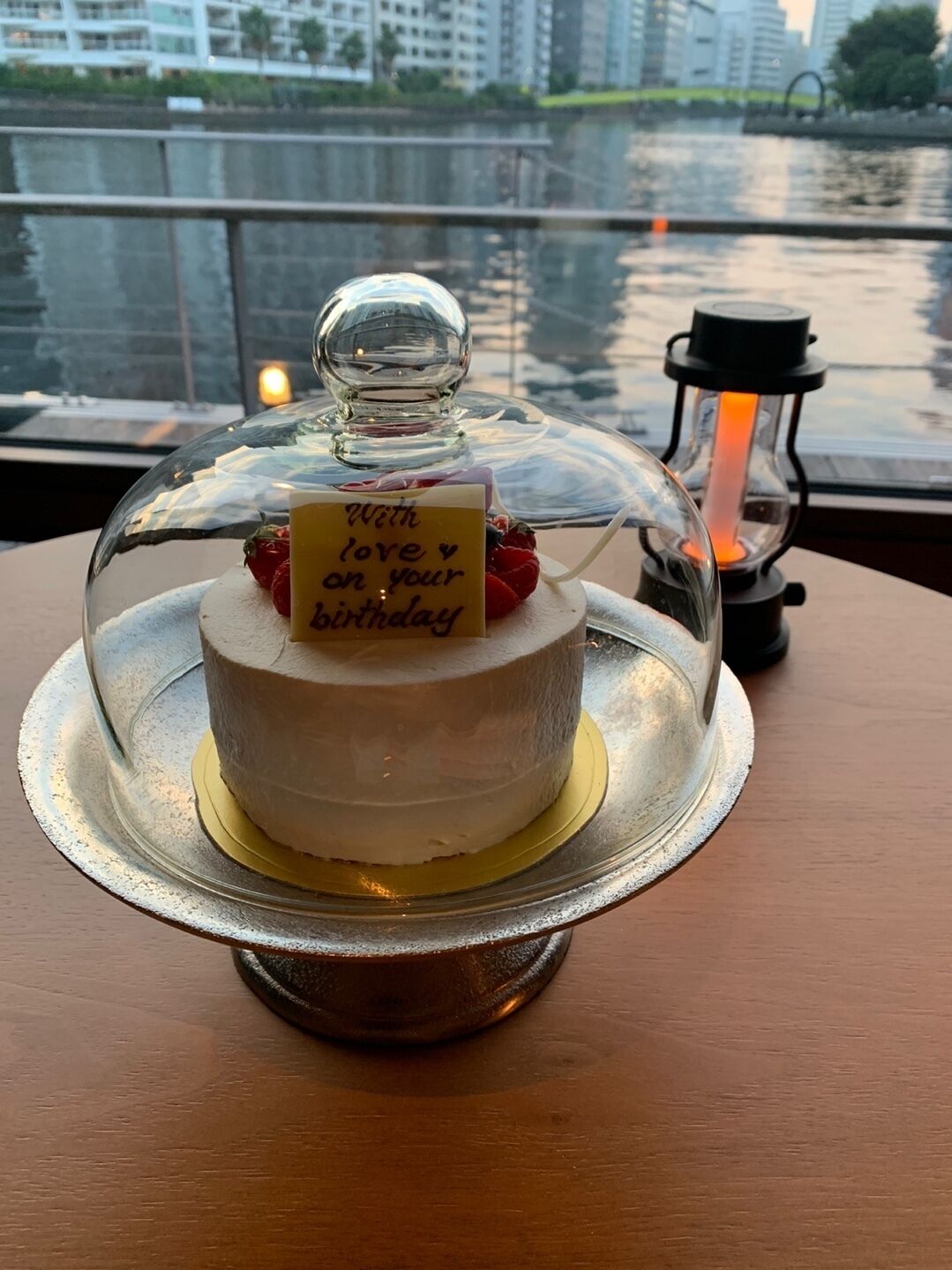 Un gâteau d’anniversaire avec un message, posé sur une table près d’une fenêtre donnant sur un plan d’eau.