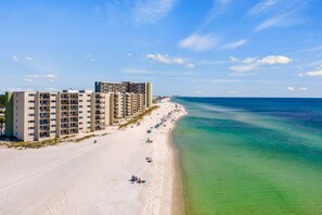 Ein Strandhotel mit mehreren Etagen, einem sandigen Strand und einem klaren, blauen Meer.