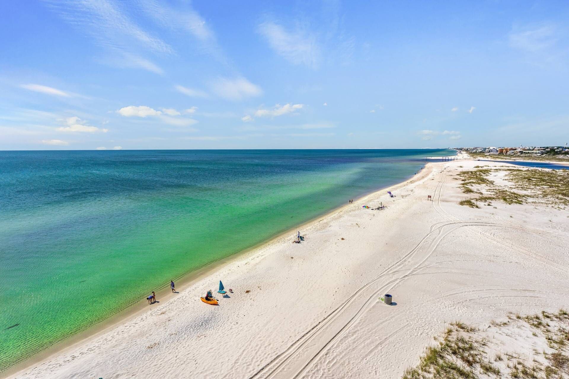 A beach with clear turquoise water, a sandy shore, and a few people and beach chairs.